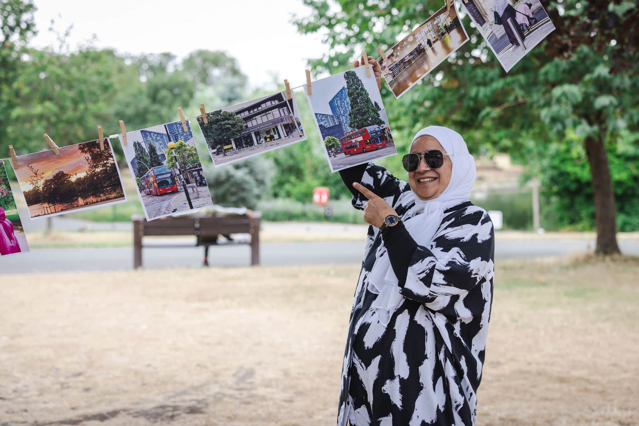 Woman wearing bright clothing and sunglasses holding onto a photograph outside in a park