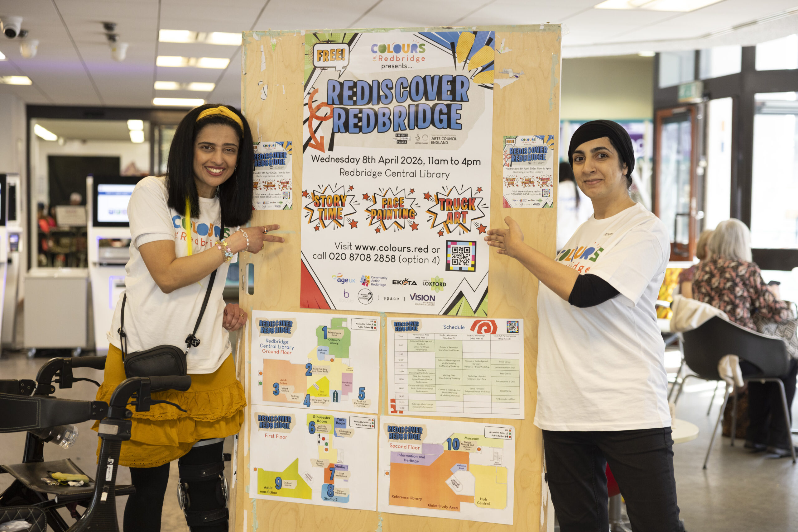Two Colours of Redbridge staff standing by the Redsicover Redbridge poster